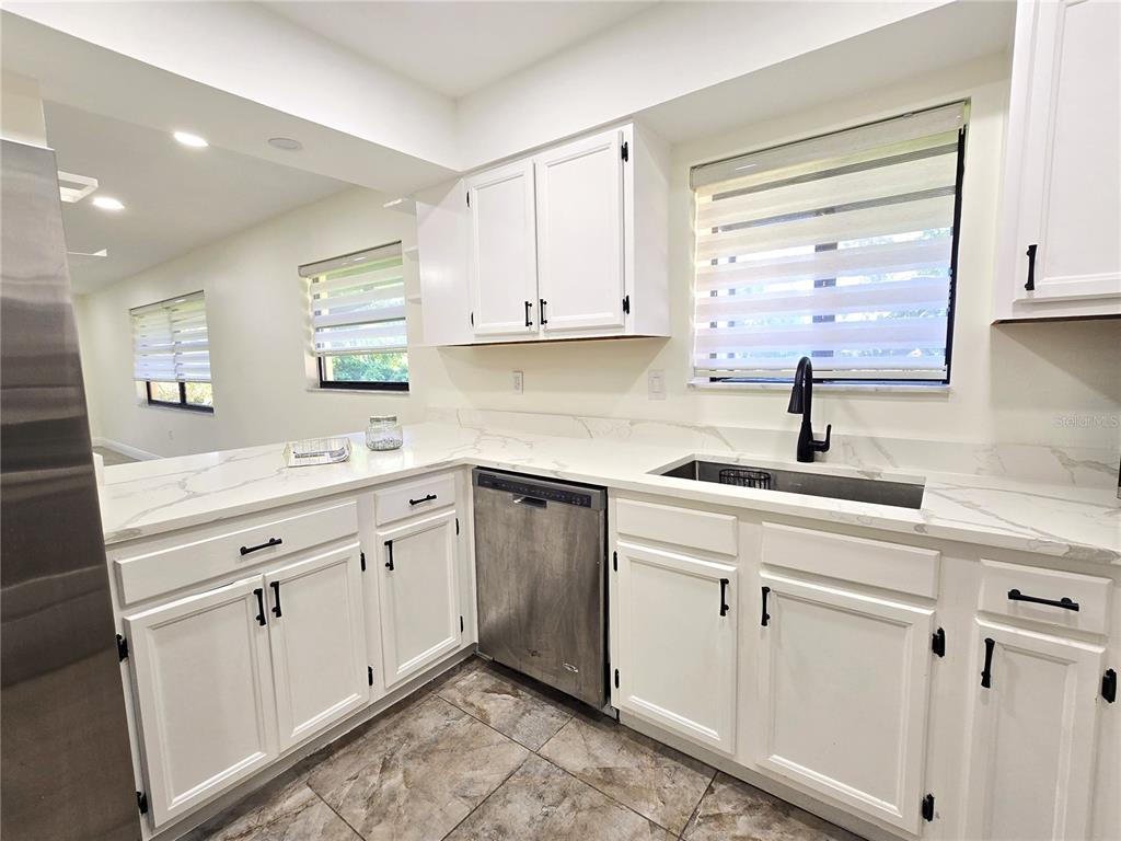 A kitchen features white cabinets, marble-look countertops, stainless steel appliances, and tile flooring — 2009 HAMMOCK PINE BOULEVARD UNIT 2009, CLEARWATER, FL