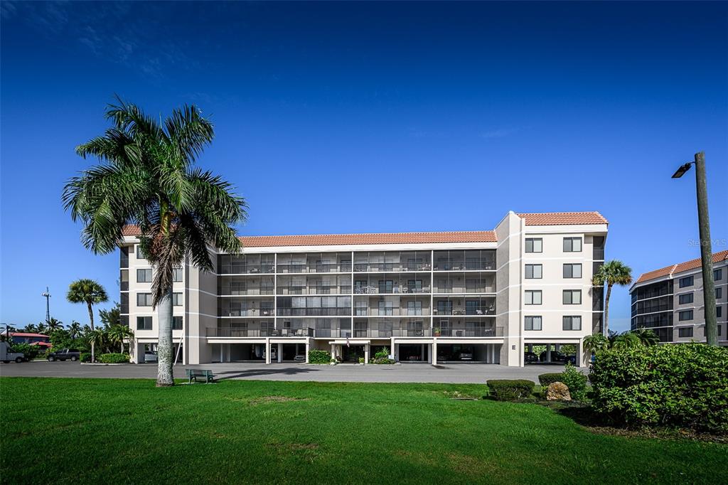 A multi-story apartment building with a palm tree and a grassy lawn in front — 25188 MARION AVENUE UNIT E104, PUNTA GORDA, FL