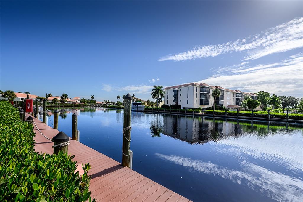 A wooden dock runs alongside a canal with a multi-story apartment building in the background — 25188 MARION AVENUE UNIT E104, PUNTA GORDA, FL