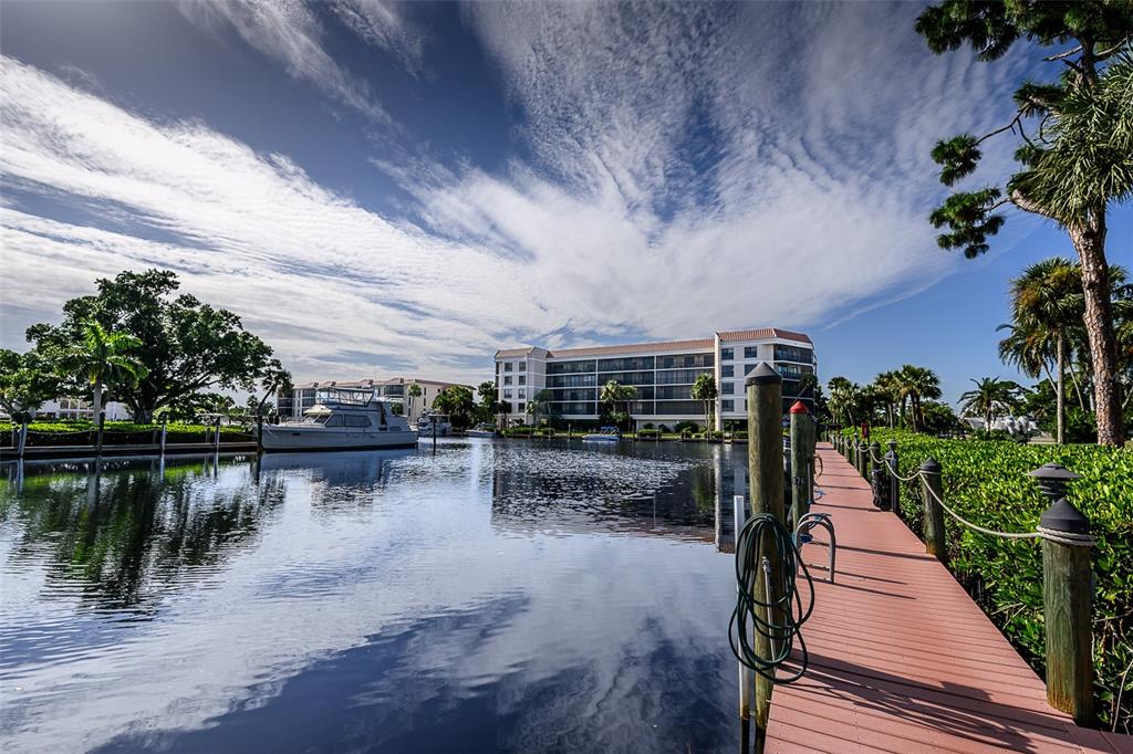 A wooden dock extends into a calm canal toward a multi-story apartment building and boat — 25188 MARION AVENUE UNIT E104, PUNTA GORDA, FL