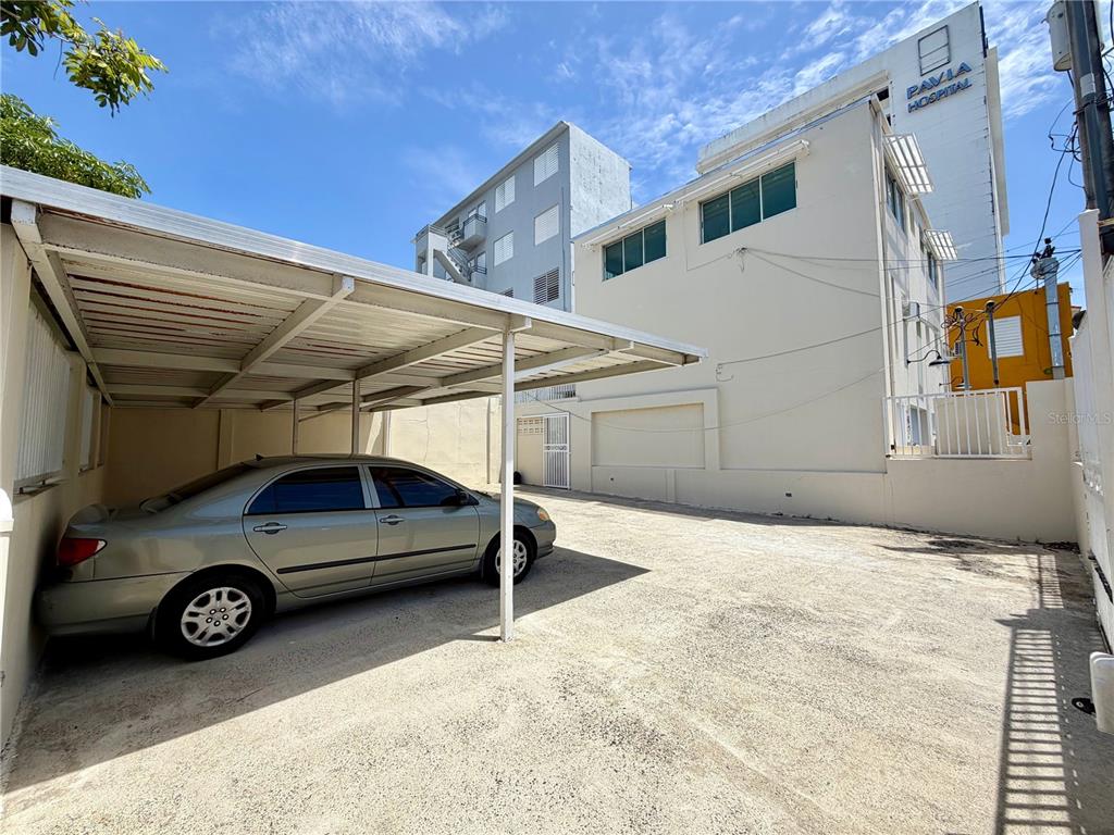 A silver sedan is parked under a metal carport next to a multi-story building — 704 SANCHEZ UNIT 702, SAN JUAN, PR
