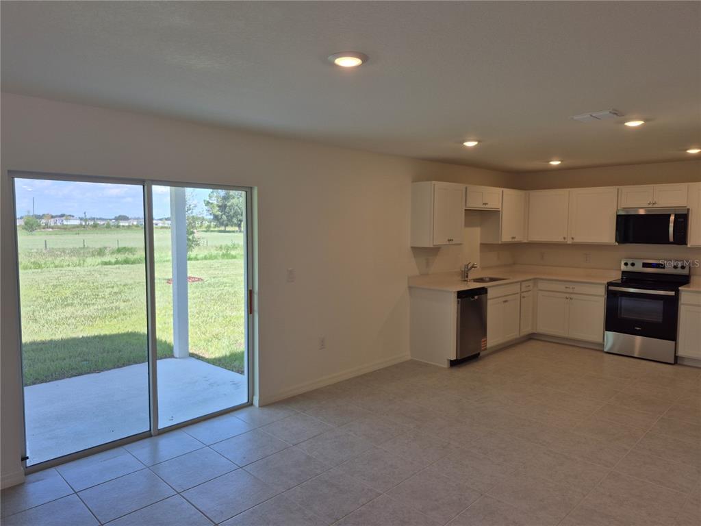 A kitchen features white cabinets, stainless steel appliances, light countertops, and light-colored tile flooring — 8813 PINE BARK WAY, WILDWOOD, FL