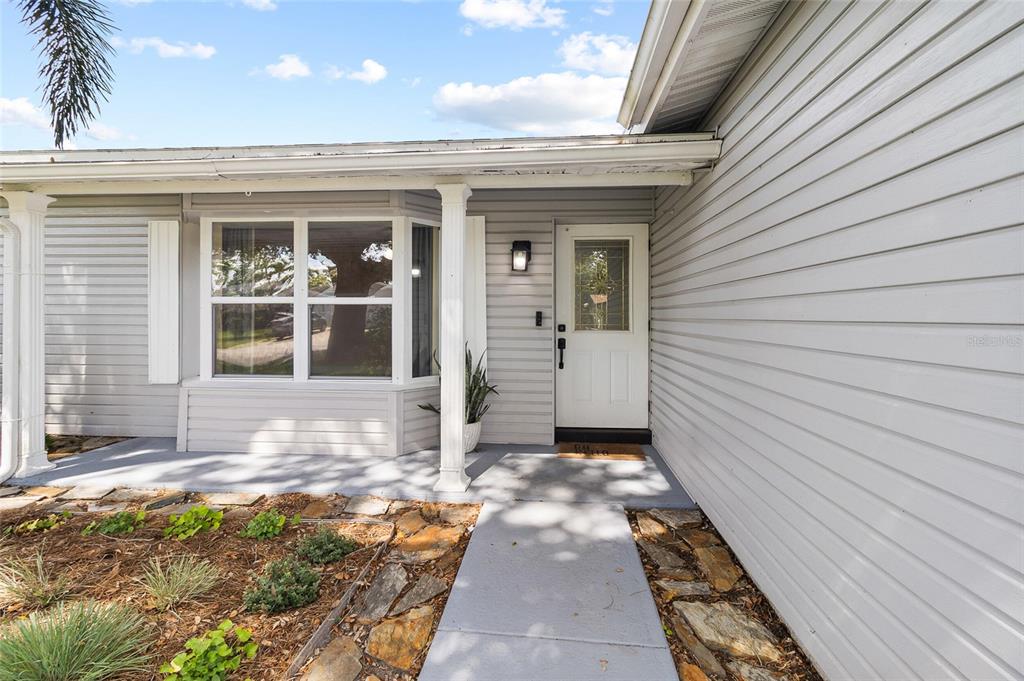 The exterior of a house features gray siding, a white front door, and a stone walkway — 11290 116TH STREET, LARGO, FL