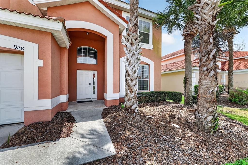The exterior of a two-story orange stucco house features a white front door and palms — 928 SOLANA CIRCLE, DAVENPORT, FL