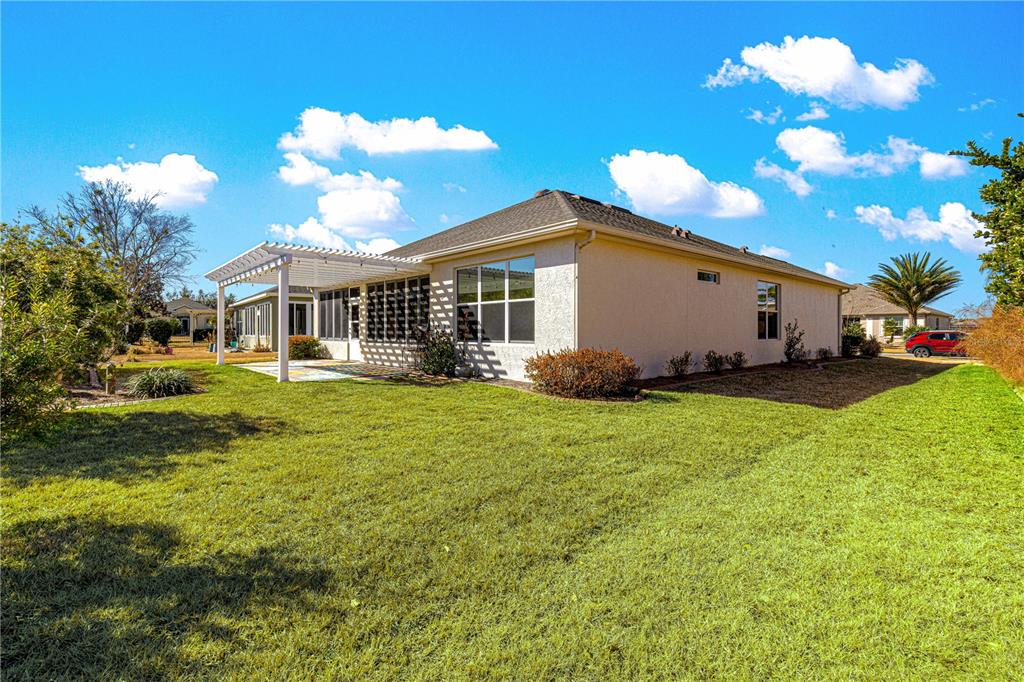 A single-story house with a screened-in patio and a pergola sits on a grassy lawn — 9256 SW 66TH LOOP, OCALA, FL