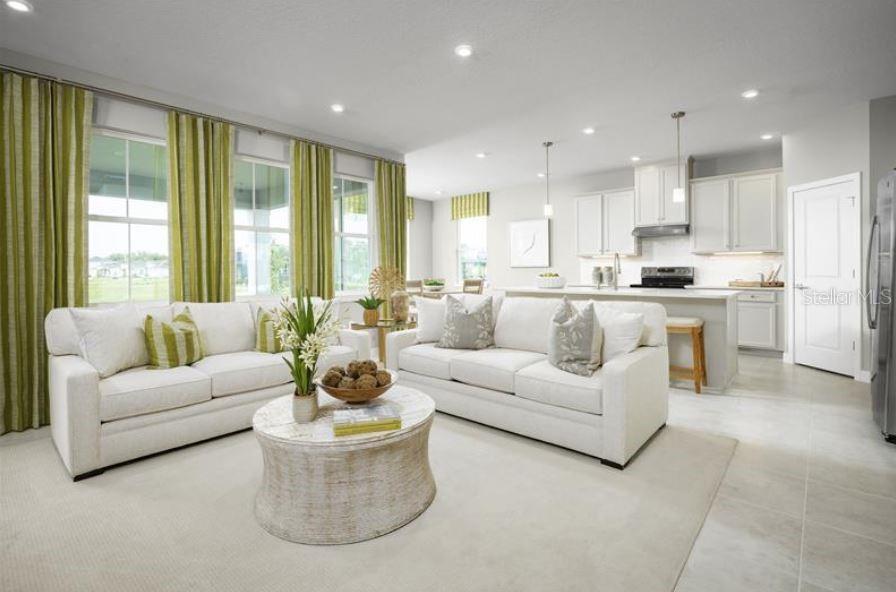 A bright open-concept living room with white sofas, a round coffee table, and kitchen area — 8343 WENDY ROSE WAY, LEESBURG, FL
