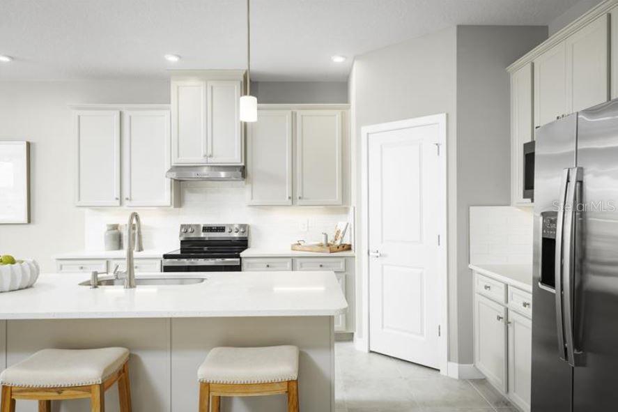 A modern kitchen features white cabinets, stainless steel appliances, and a large central island — 8343 WENDY ROSE WAY, LEESBURG, FL