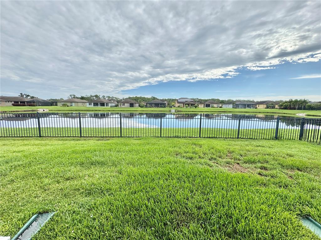 A grassy backyard features a black metal fence overlooking a pond and residential houses — 9720 58TH STREET E, PARRISH, FL
