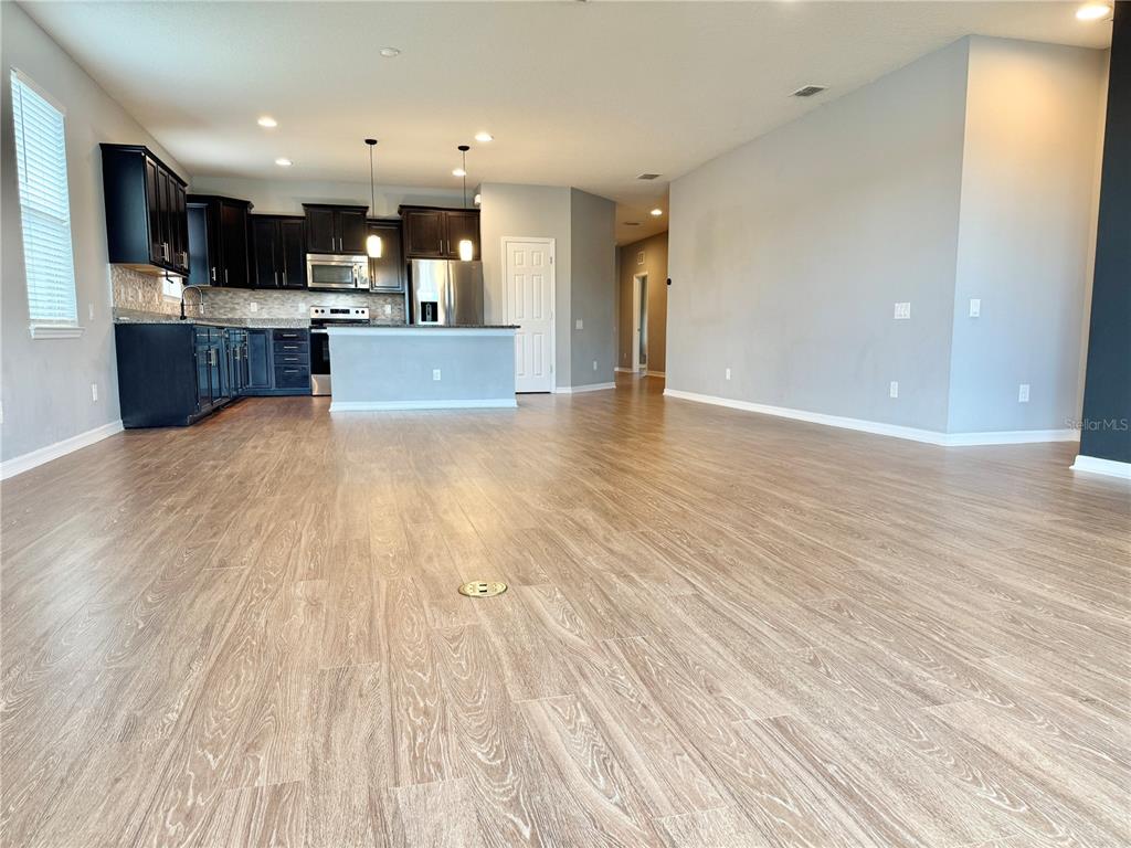 An open-concept kitchen with dark cabinets and a central island overlooks a large living area — 9720 58TH STREET E, PARRISH, FL