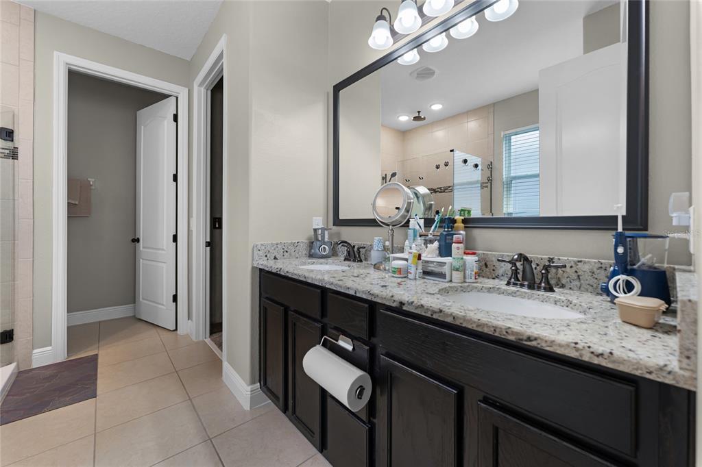 A bathroom features a double vanity with dark cabinets, granite countertops, and a large mirror — 4920 BLANCHE COURT, ST CLOUD, FL
