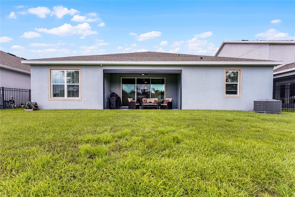 The back exterior of a single-story house features a covered patio and a grassy yard — 4920 BLANCHE COURT, ST CLOUD, FL