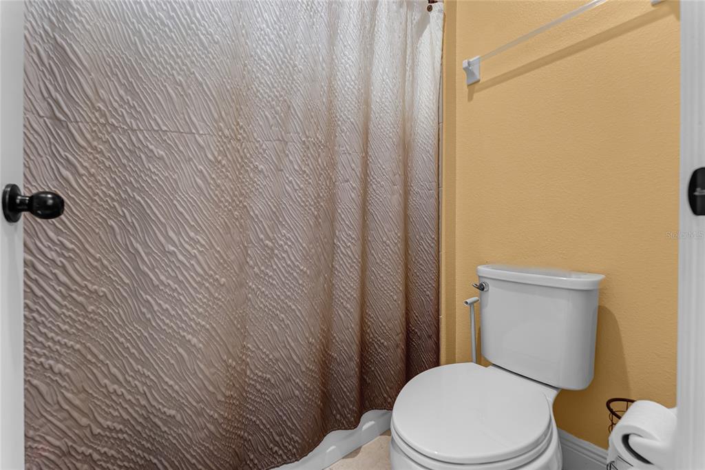 A bathroom features a white toilet, a textured ombre shower curtain, and yellow walls — 4920 BLANCHE COURT, ST CLOUD, FL