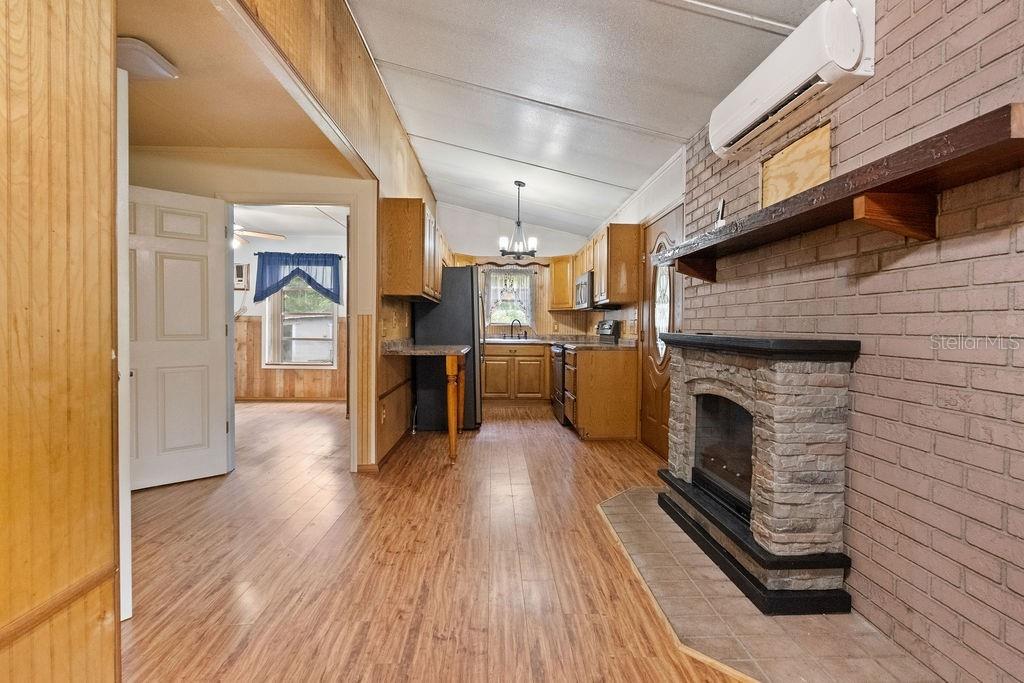 A kitchen and living area feature wood-paneled walls, wood flooring, and a stone fireplace — 4050 SE 170TH PLACE, INGLIS, FL