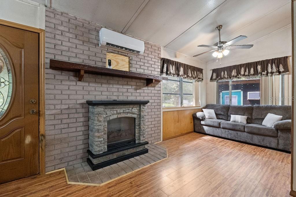 A living room features a brick fireplace, a wall-mounted air conditioner, and a gray sofa — 4050 SE 170TH PLACE, INGLIS, FL