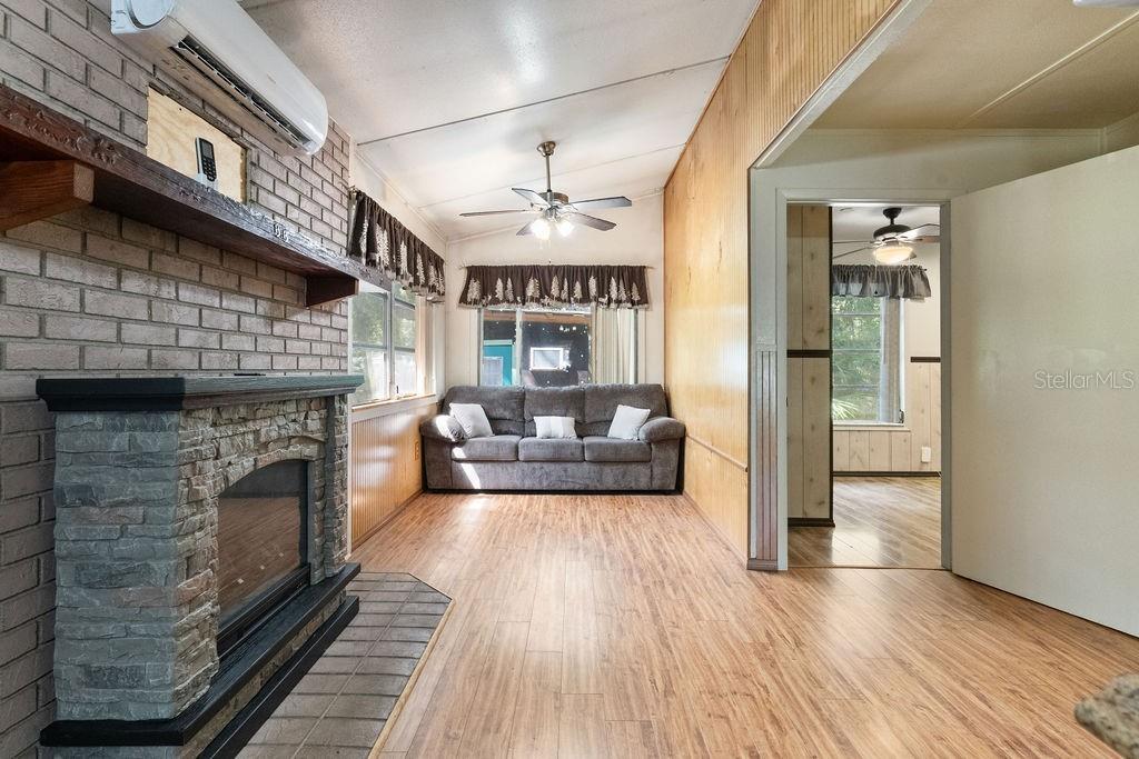 A living room features a stone fireplace, wood-paneled walls, wood-look flooring, and a gray sofa — 4050 SE 170TH PLACE, INGLIS, FL