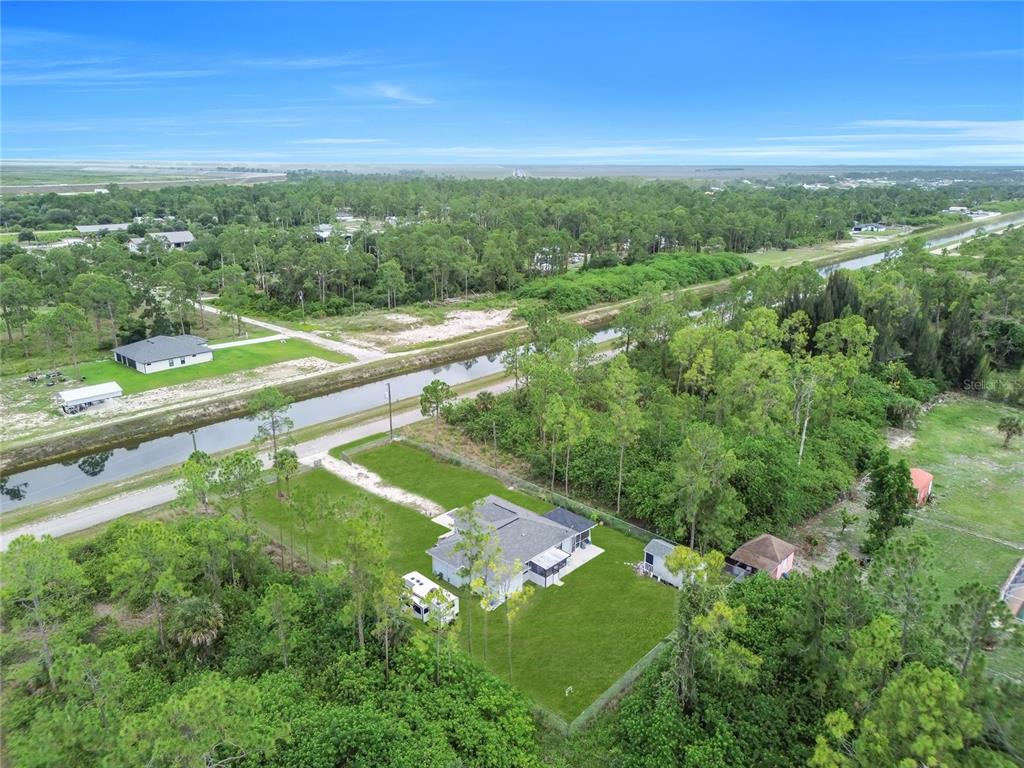 An aerial view shows a house with a large yard, a camper, and a canal — 2021 HINES AVENUE, ALVA, FL