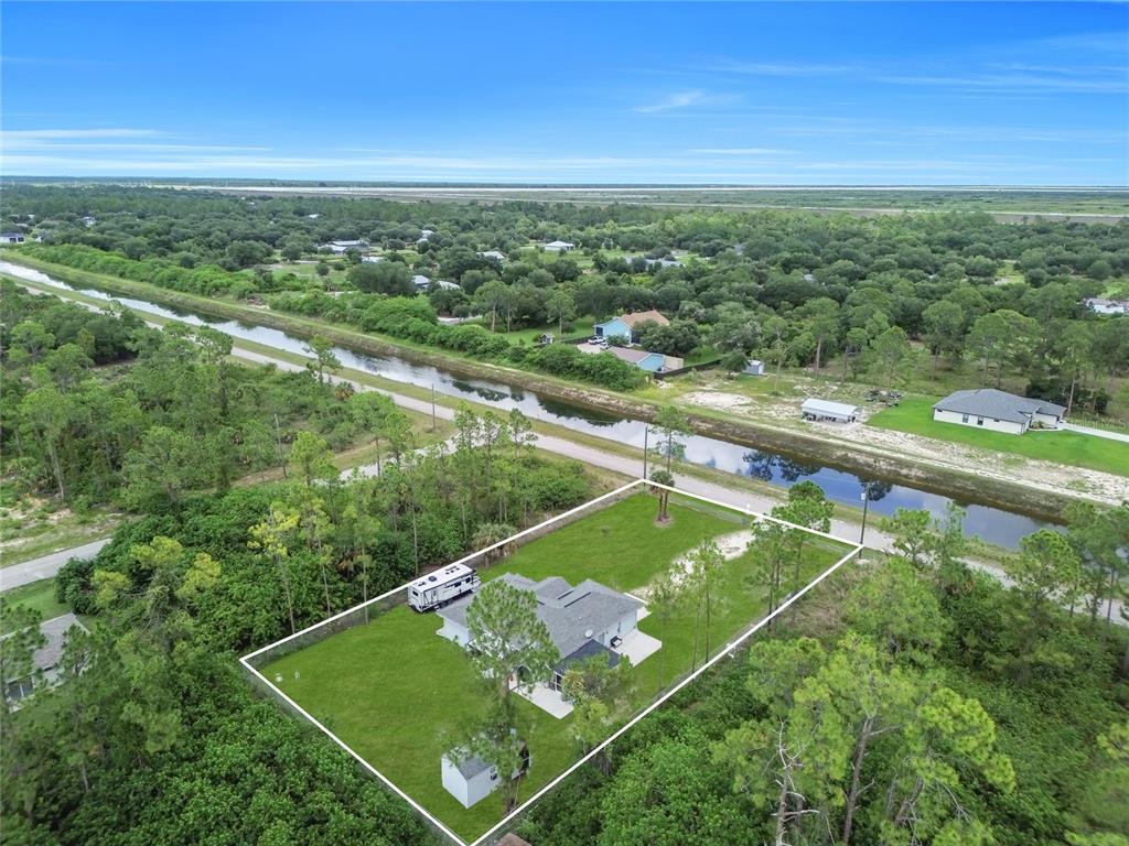 An aerial view shows a single-story house with a fenced yard next to a canal — 2021 HINES AVENUE, ALVA, FL