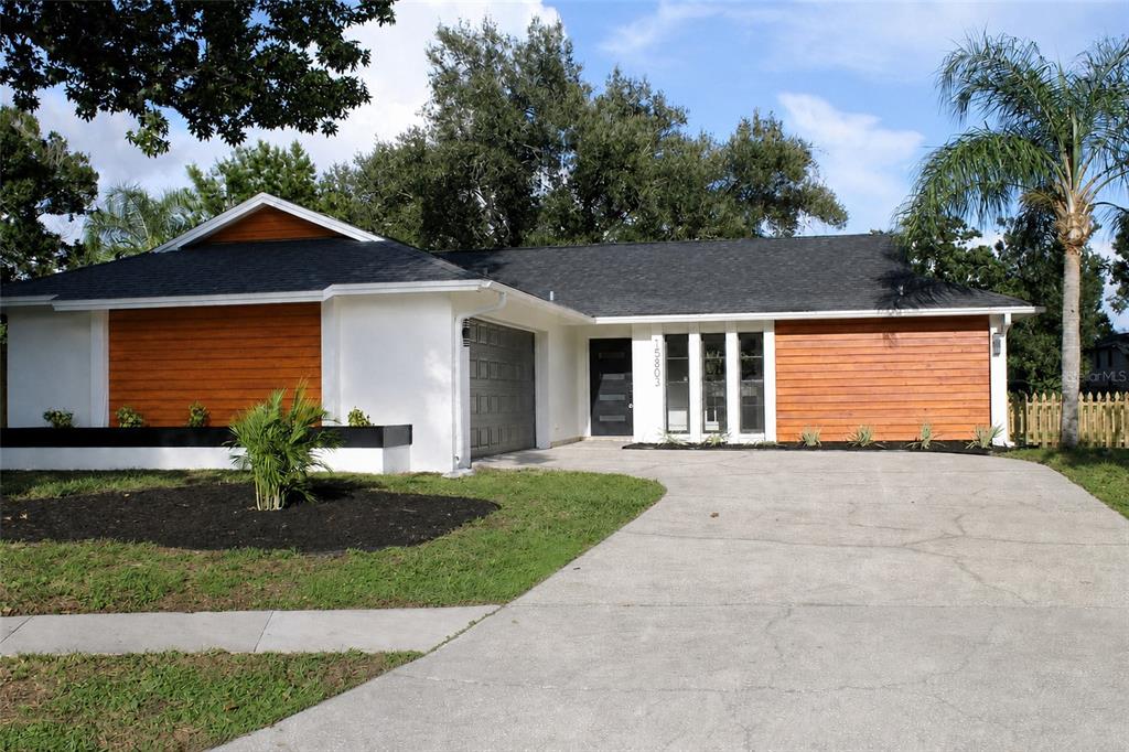A single-story house features white walls, horizontal wood siding, a dark roof, and a concrete driveway — 15803 IRONWARE PLACE, TAMPA, FL