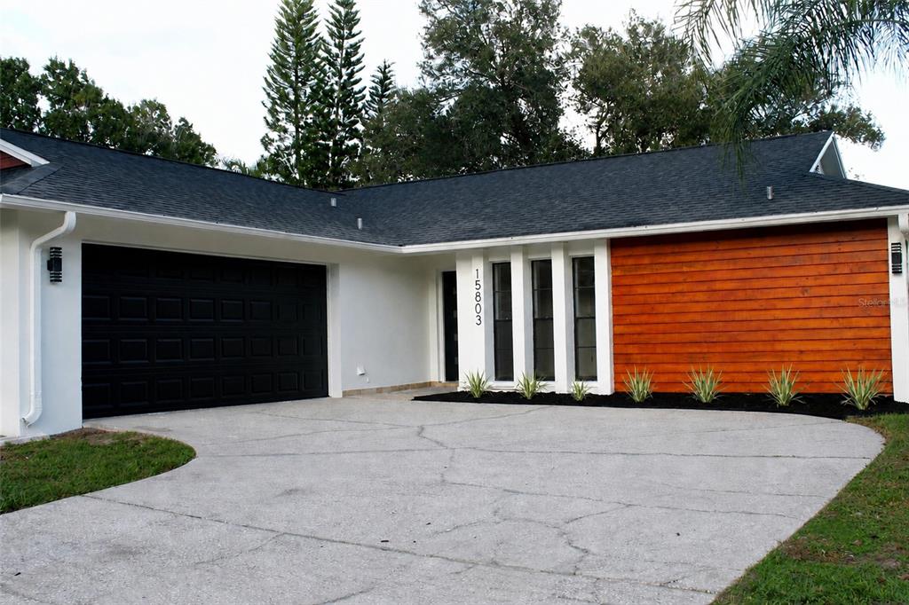 A single-story house exterior features a black garage door, wood siding, and a concrete driveway — 15803 IRONWARE PLACE, TAMPA, FL