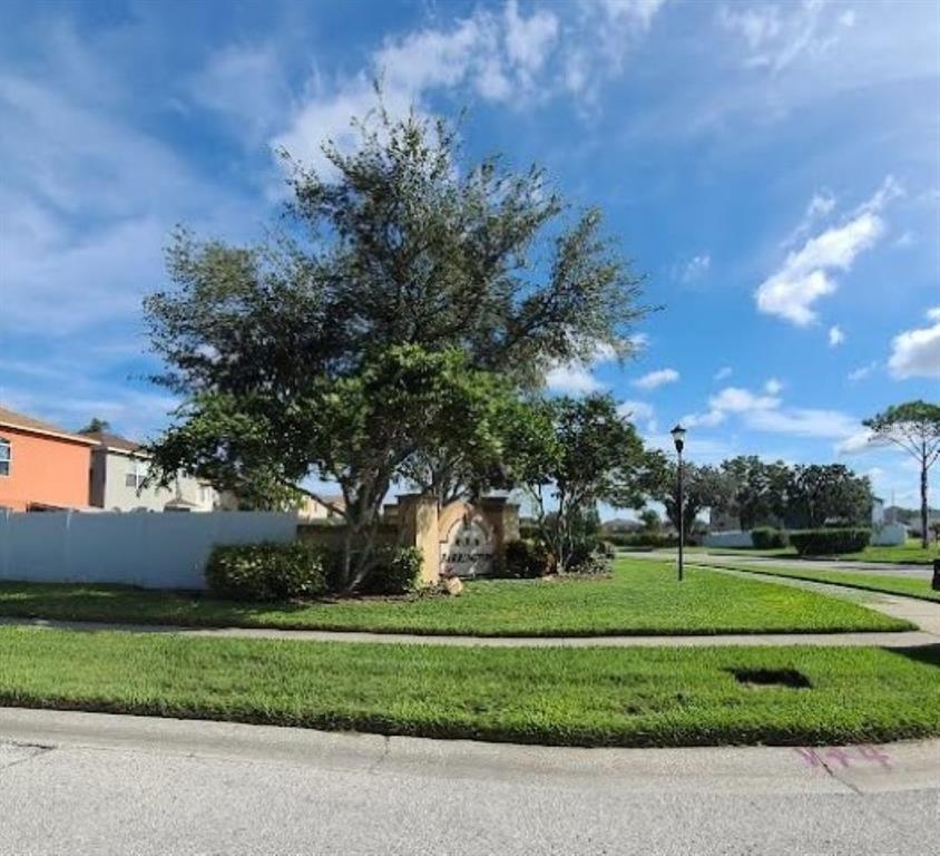 A large tree stands behind a neighborhood entrance sign on a grassy corner lot — 1501 RINCON DRIVE, WESLEY CHAPEL, FL