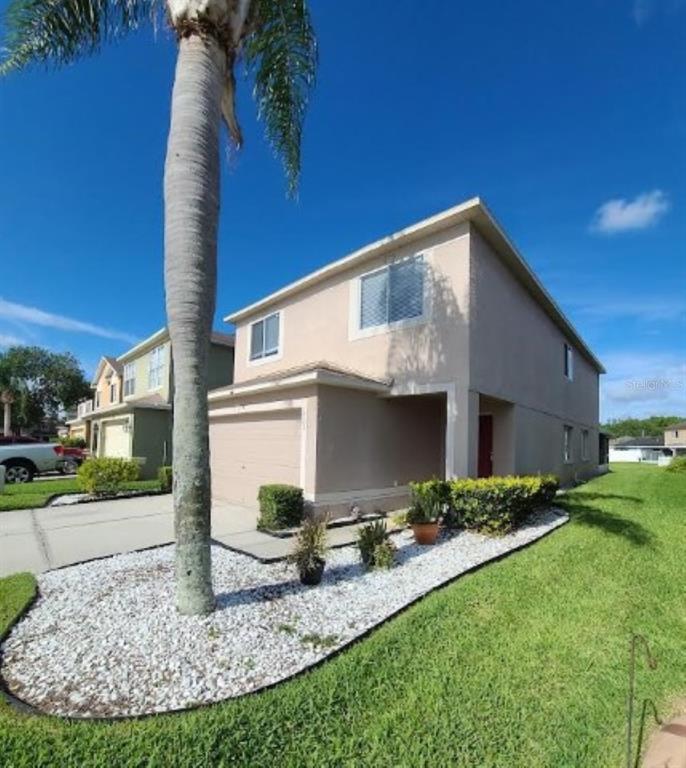 A two-story beige house with a garage, a palm tree, and a white rock garden — 1501 RINCON DRIVE, WESLEY CHAPEL, FL