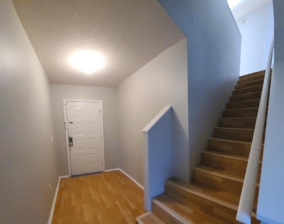 An entryway with light wood flooring, a white front door, and a staircase leading upward — 1501 RINCON DRIVE, WESLEY CHAPEL, FL