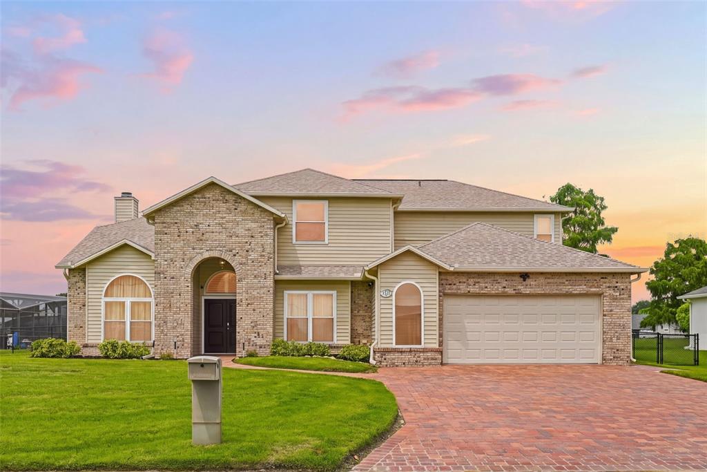 A two-story suburban home features tan siding, a brick facade, and a paved driveway — 1791 LISA LANE, KISSIMMEE, FL