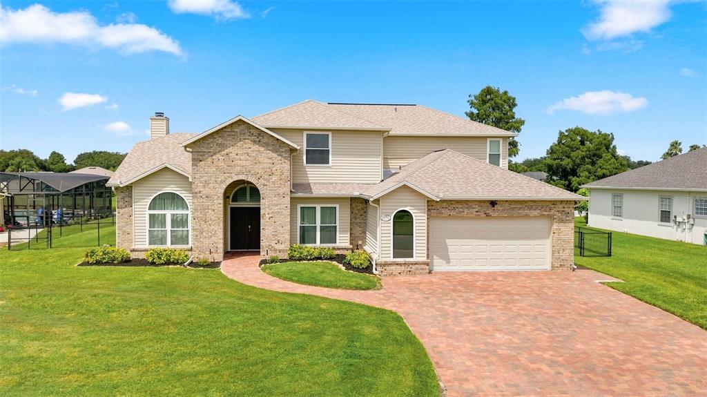 A two-story house with tan siding, a brick facade, and a paved driveway — 1791 LISA LANE, KISSIMMEE, FL