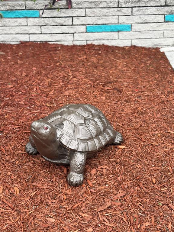A decorative turtle statue sits on a bed of brown mulch in front of a wall — 723 ROMA ROAD, VENICE, FL