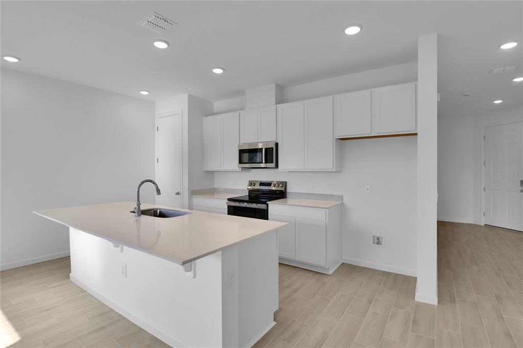 A modern kitchen features white cabinets, a central island with a sink, and light flooring — 762 LAKE DELL AVENUE, DUNDEE, FL