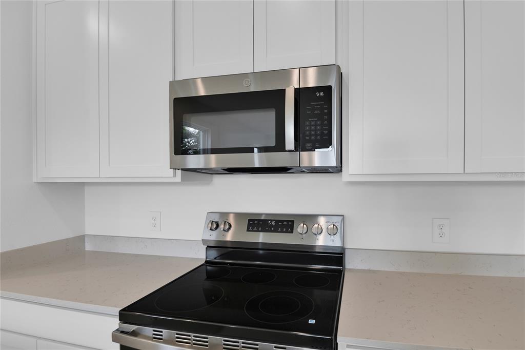 A stainless steel microwave and electric range are installed between white cabinets and quartz countertops — 762 LAKE DELL AVENUE, DUNDEE, FL