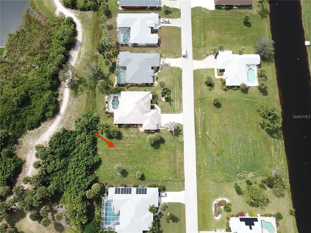 An aerial view shows a vacant residential lot situated between two houses and a wooded area — 54 MARKER ROAD, ROTONDA WEST, FL