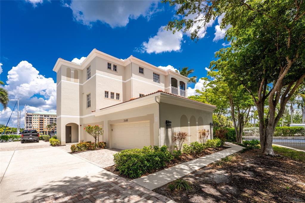 A three-story beige stucco house features a two-car garage and a paved driveway — 3485 SUNSET KEY CIRCLE UNIT 101, PUNTA GORDA, FL
