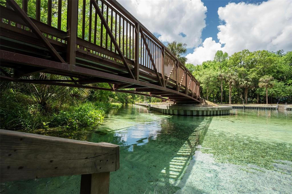A metal pedestrian bridge spans a clear, shallow spring surrounded by lush green trees — KELLY PARK ROAD E, APOPKA, FL