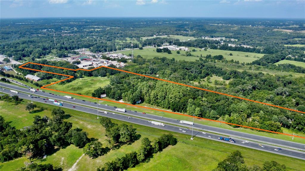 An aerial view shows a wooded plot of land outlined in orange next to a highway — 7820 NW 42ND AVENUE RD, OCALA, FL