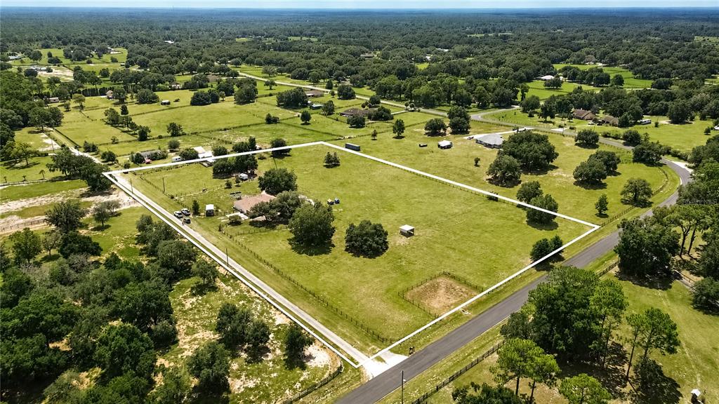 An aerial view shows a fenced rural property with a house, trees, and open pasture — 10525 SW 129TH TERRACE ROAD, DUNNELLON, FL