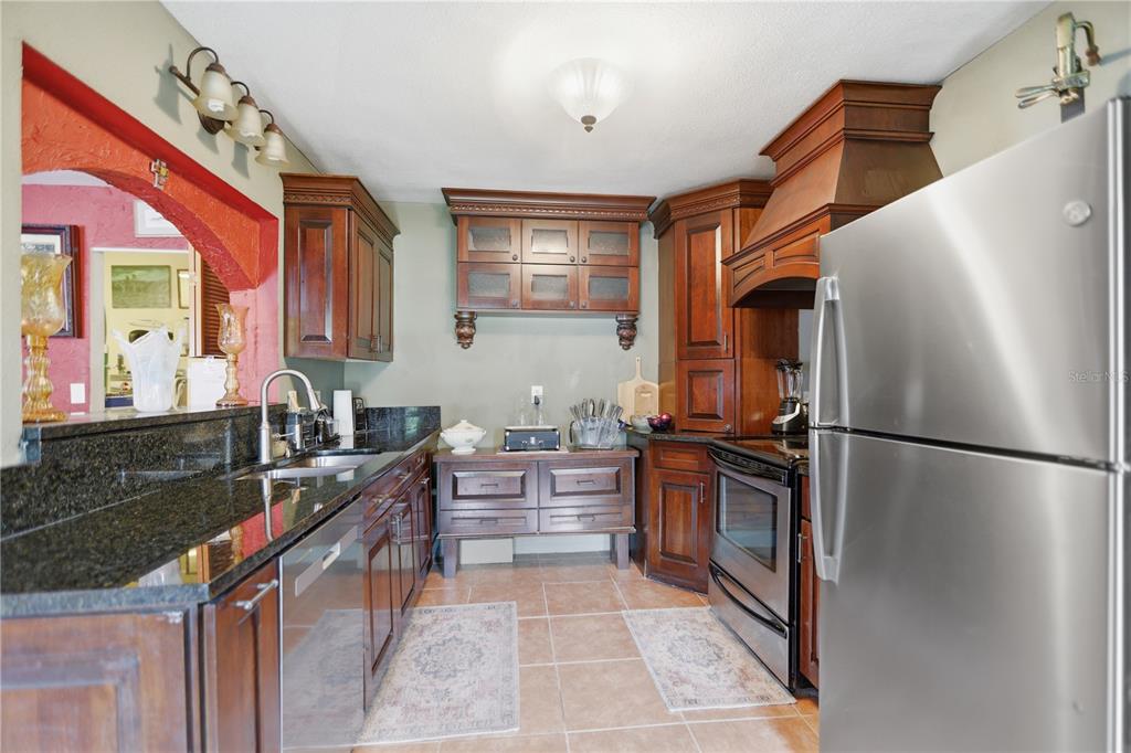 A kitchen features dark wood cabinets, granite countertops, stainless steel appliances, and tile flooring — 120 VALENCIA ROAD, ROCKLEDGE, FL