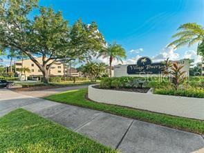 A sign for Village Towers stands in front of a multi-story apartment building and trees — 13608 S VILLAGE DRIVE UNIT 8203, TAMPA, FL