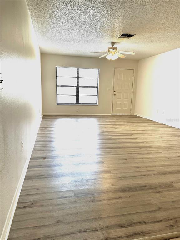An empty room with light wood-look flooring, a ceiling fan, a window, and a door — 13608 S VILLAGE DRIVE UNIT 8203, TAMPA, FL
