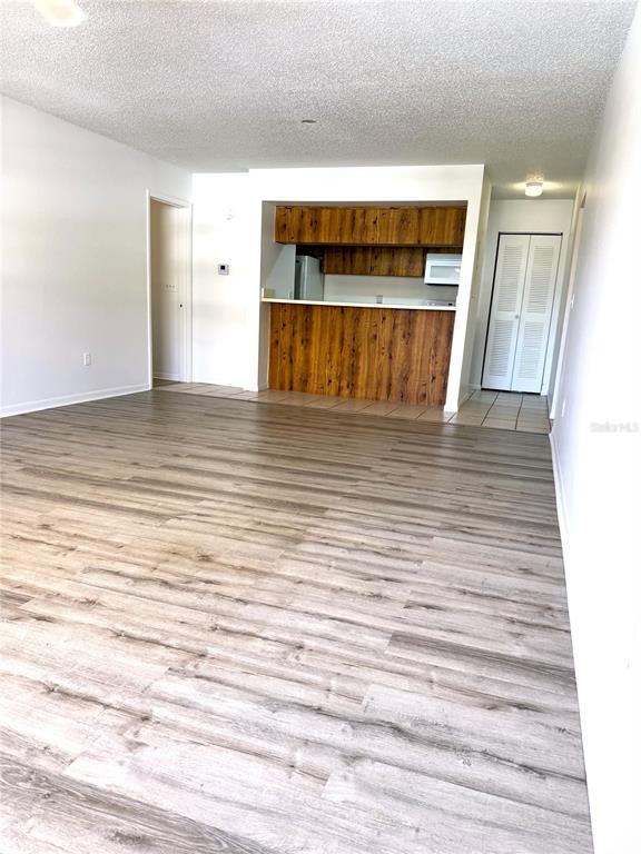 A living room with wood-look flooring leads to a kitchen featuring wood-paneled cabinets and counters — 13608 S VILLAGE DRIVE UNIT 8203, TAMPA, FL