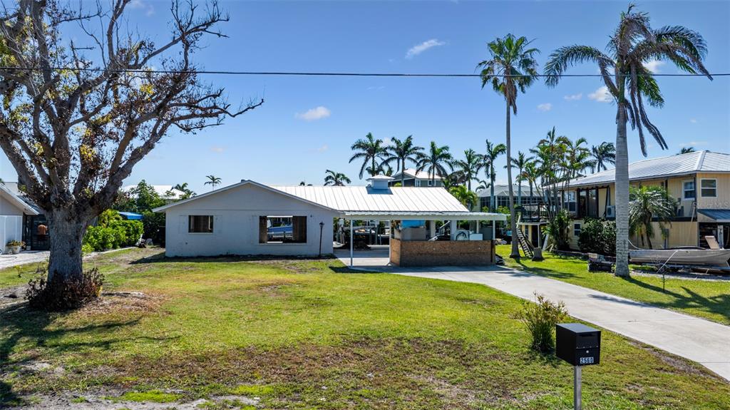 A single-story house with a metal roof and an attached carport sits on a grassy lot — 2560 BAYBREEZE STREET, ST JAMES CITY, FL