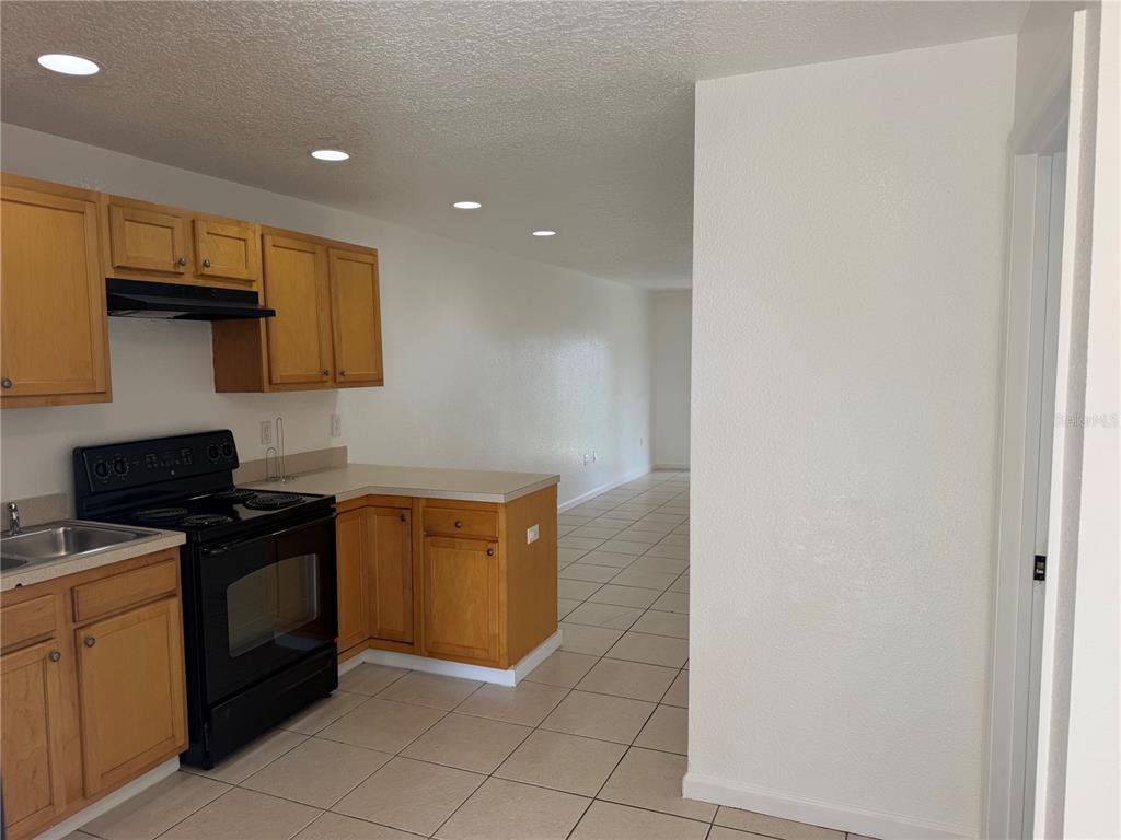 A kitchen with light wood cabinets, black appliances, and tile flooring opens to a hallway — 752 E BROOME STREET, CLERMONT, FL