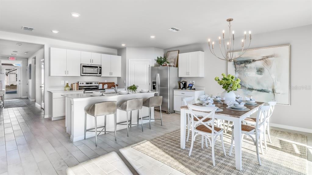 A bright, open-concept kitchen and dining area features white cabinetry, stainless appliances, and tile flooring — 1445 MABLETON DRIVE, PORT CHARLOTTE, FL