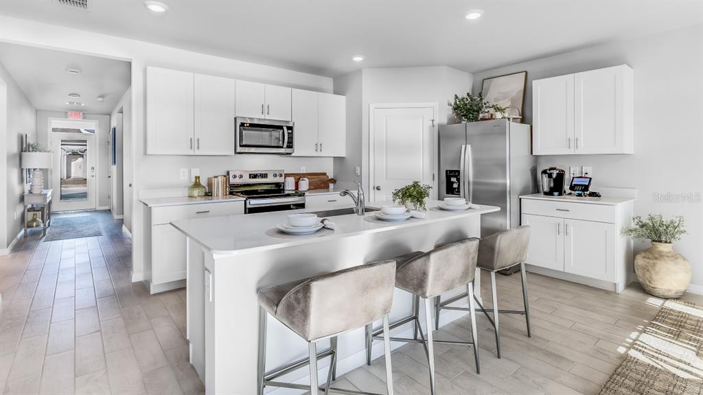 A modern kitchen features white cabinets, stainless steel appliances, a central island, and bar stools — 1445 MABLETON DRIVE, PORT CHARLOTTE, FL
