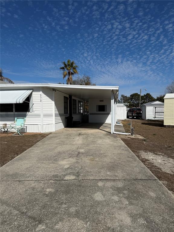 A white mobile home features a concrete driveway, a carport, and an attached storage shed — 9514 BLACK BEAR DRIVE, WEEKI WACHEE, FL