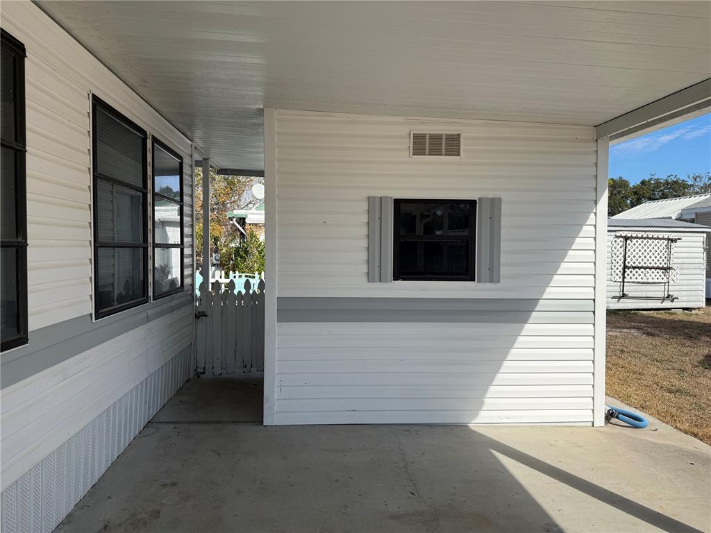 A concrete carport area features white horizontal siding, a small window, and a side gate — 9514 BLACK BEAR DRIVE, WEEKI WACHEE, FL
