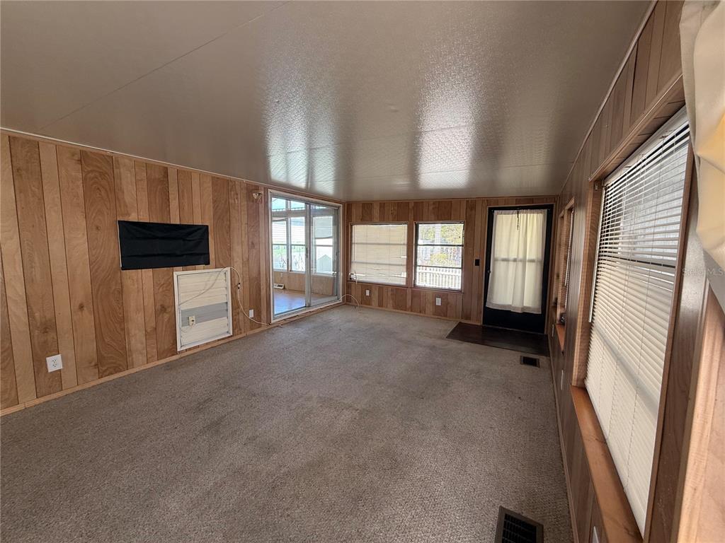 A sunroom with wood-paneled walls, carpeted flooring, multiple windows, and a glass sliding door — 9514 BLACK BEAR DRIVE, WEEKI WACHEE, FL