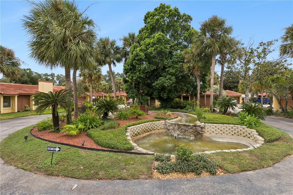A landscaped traffic circle features a stone fountain, palm trees, and surrounding single-story residential buildings — 4948 FIJI CIRCLE UNIT 3D, ORLANDO, FL