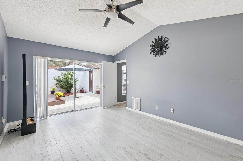 A living room with light wood-look flooring, gray walls, a ceiling fan, and sliding glass doors — 4948 FIJI CIRCLE UNIT 3D, ORLANDO, FL