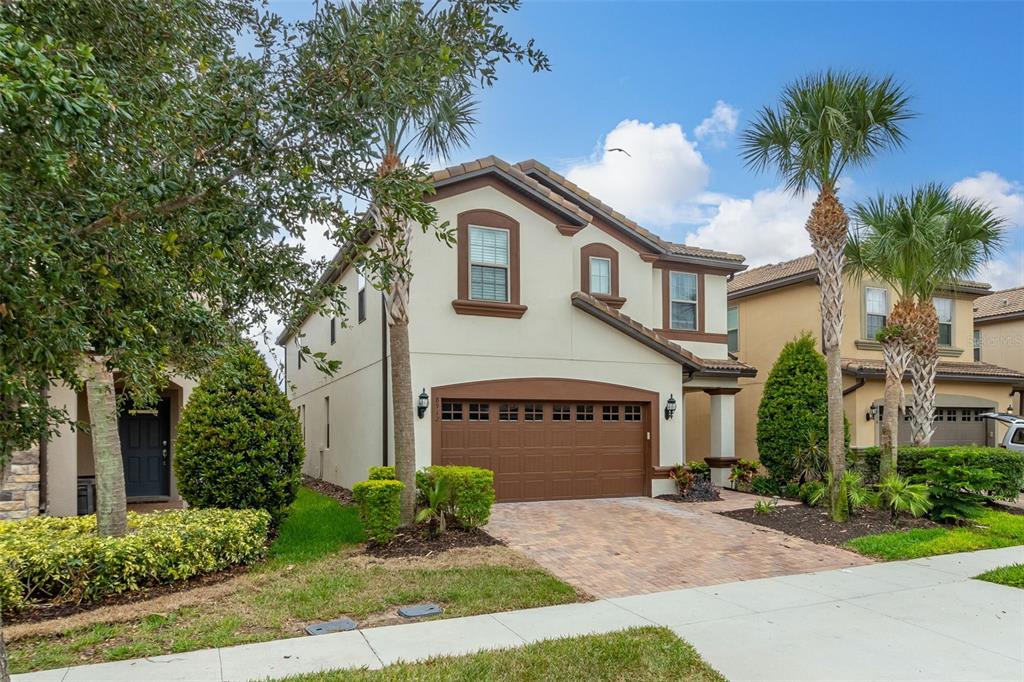 A two-story house with a tan stucco exterior, brown garage door, and a paver driveway — 8912 RHODES STREET, KISSIMMEE, FL